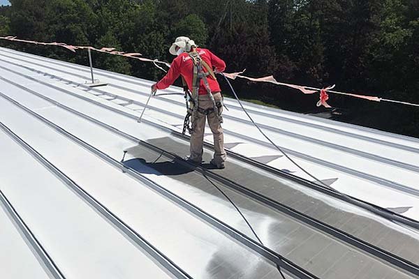 A roofer applying a roof coating on a commercial building